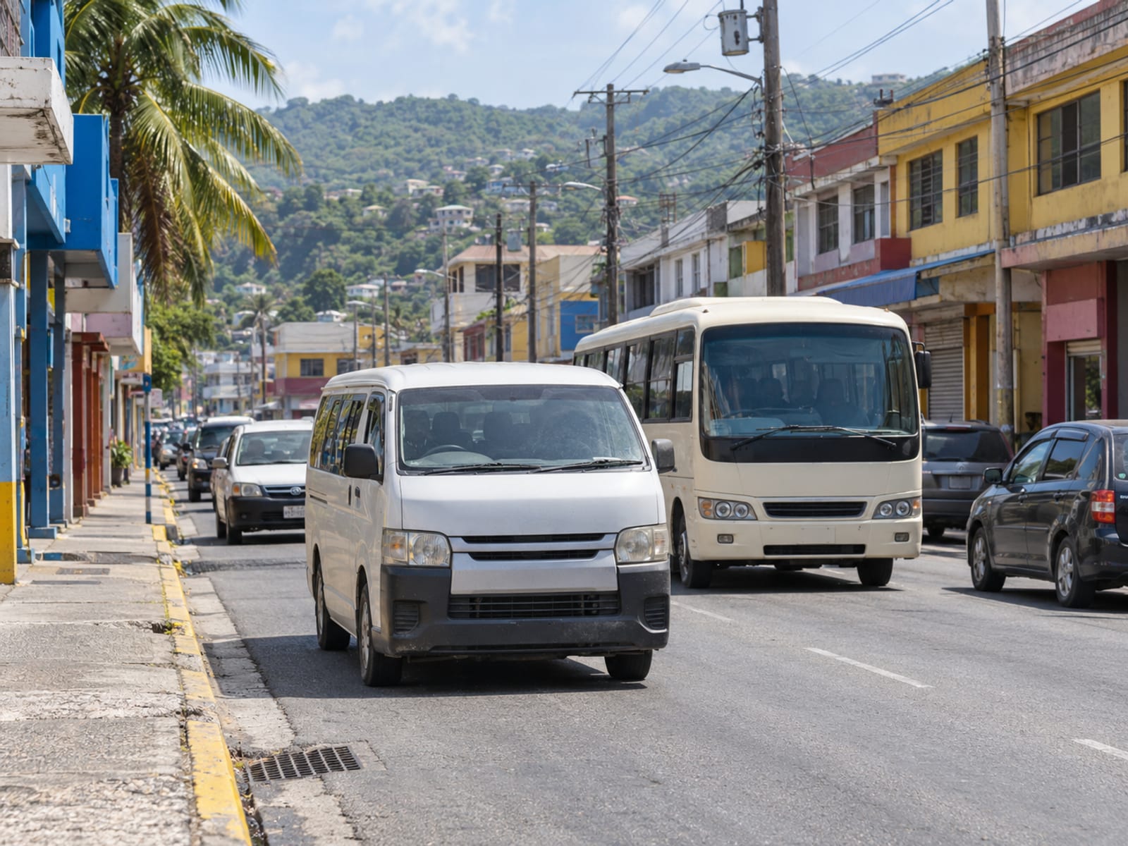 A busy road through a Jamaican town with a route taxi and a bus