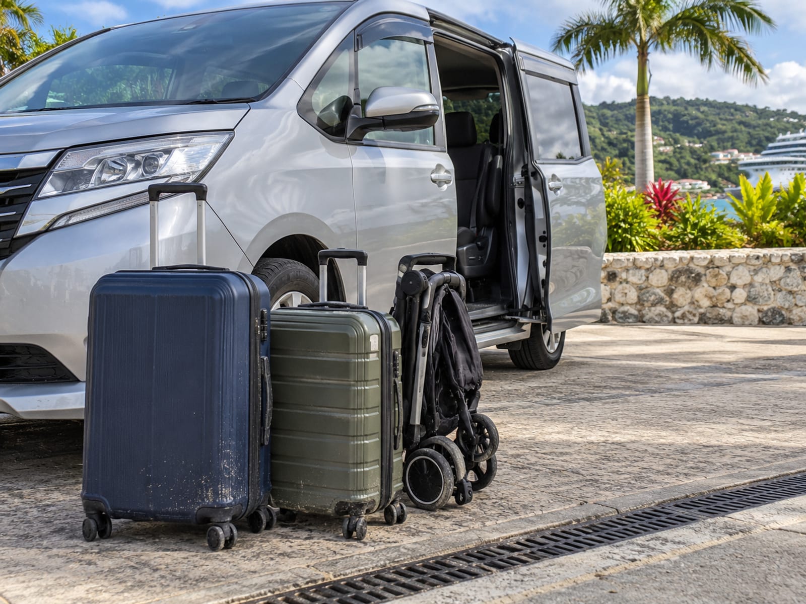 Luggage and a folded stroller beside a minivan at a pickup point