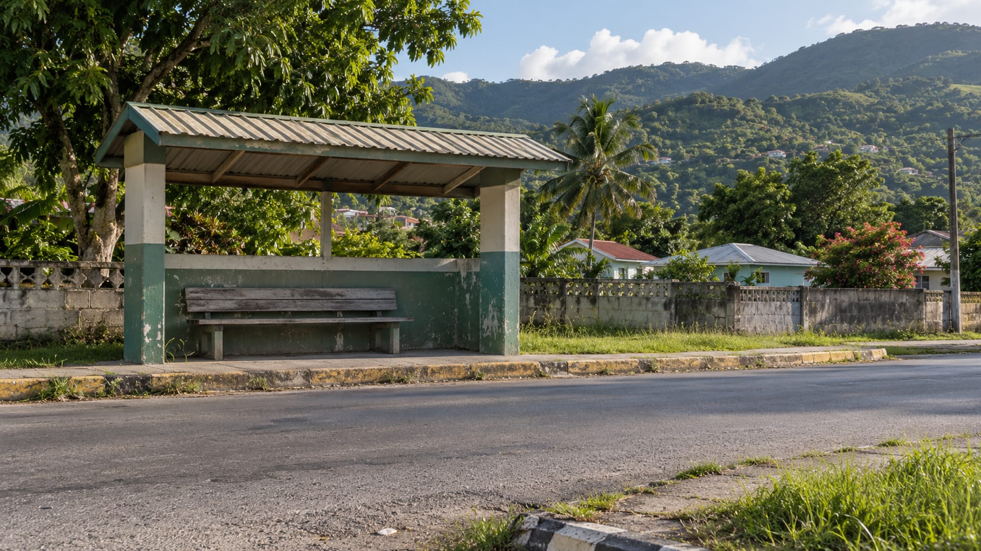 A covered roadside shelter with a bench on a quiet road below green hills