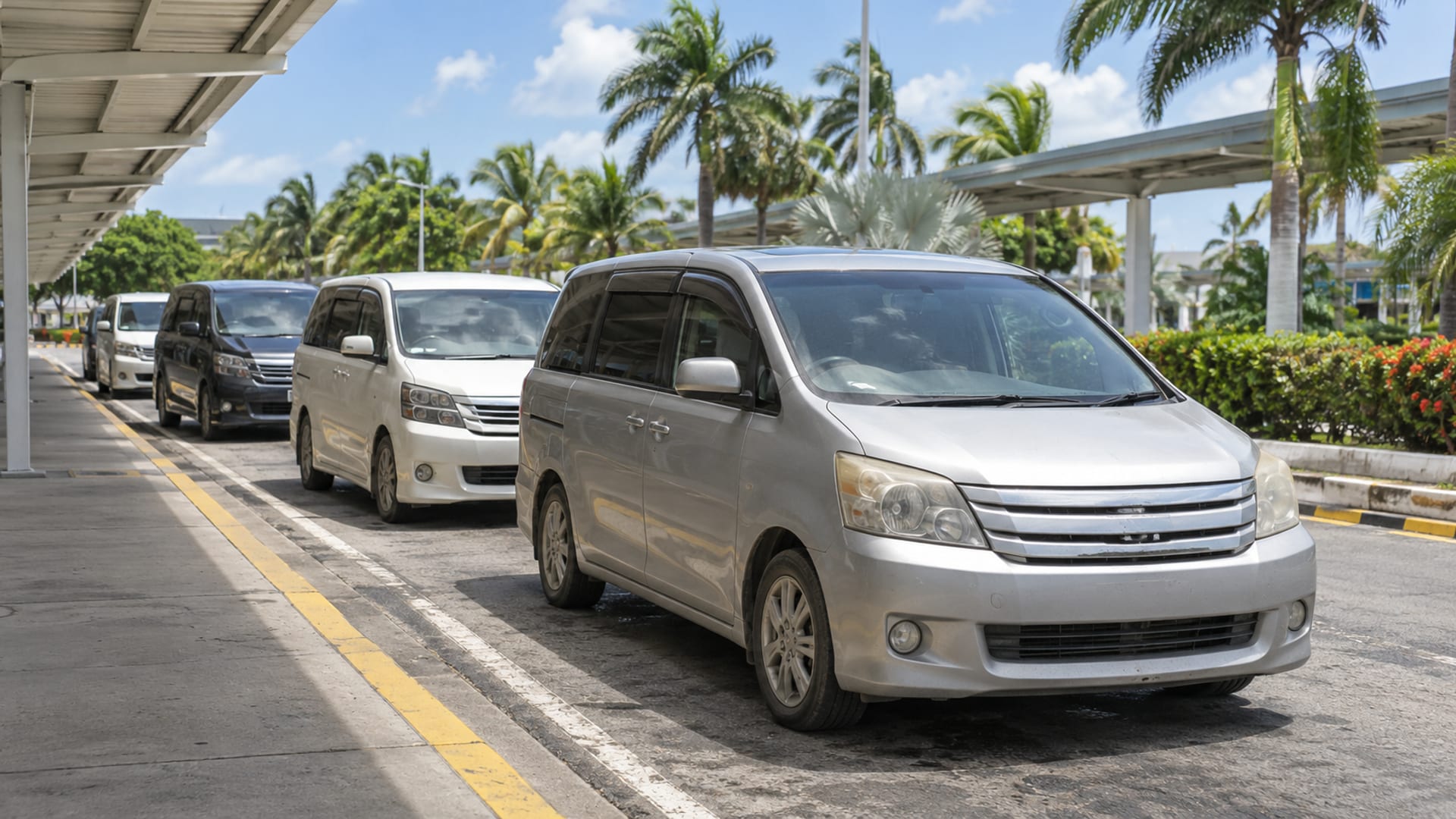 Plain minivans waiting at the kerb of an airport pickup lane