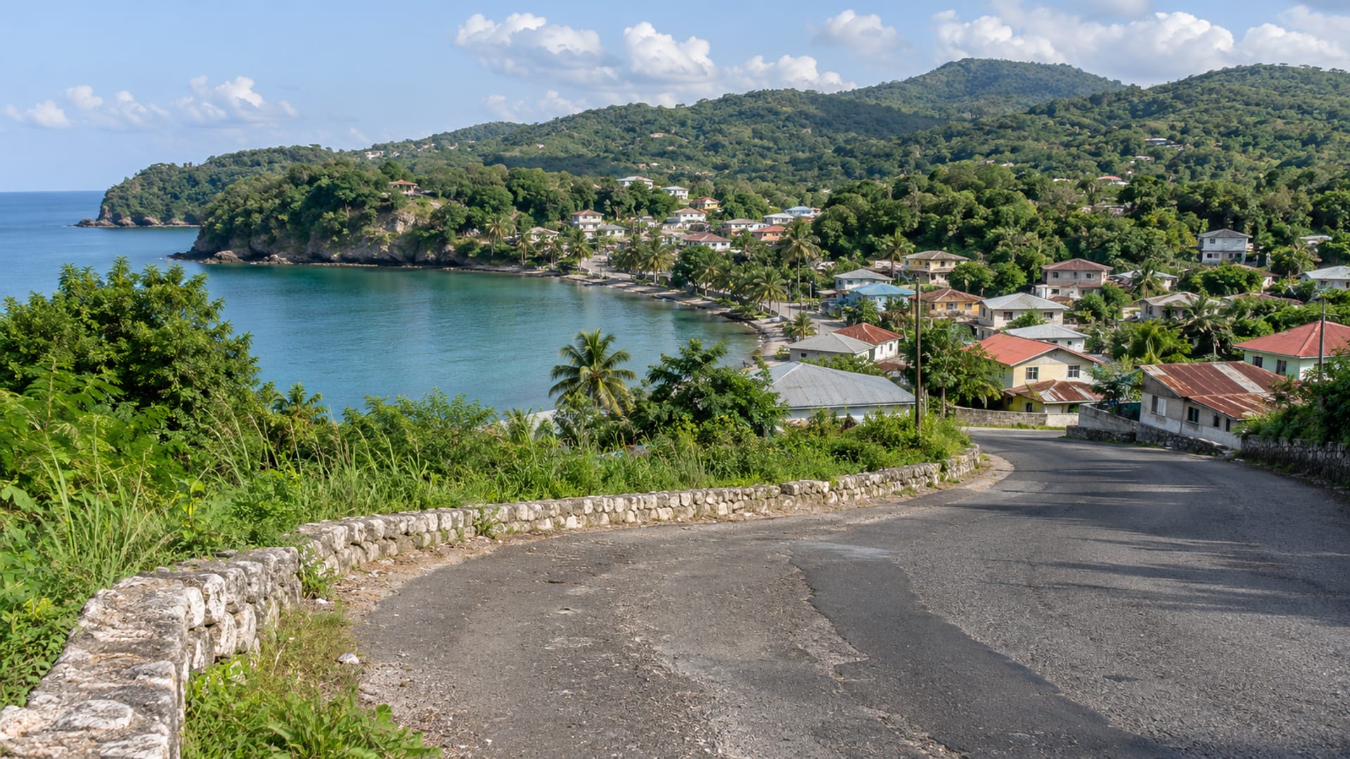 A coast road curving around a calm cove toward a small town