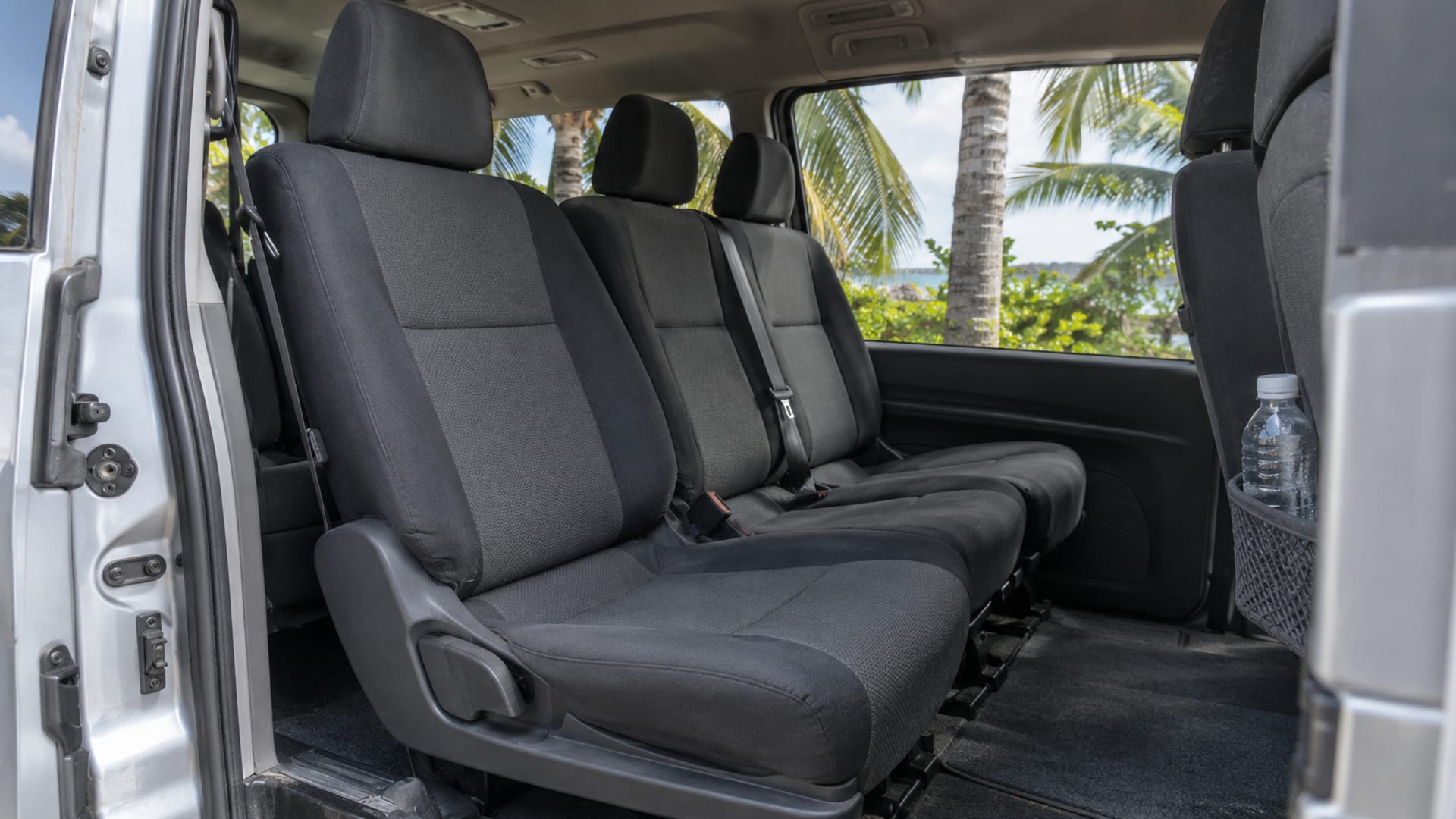 The clean interior of a minivan with its sliding door open onto palms