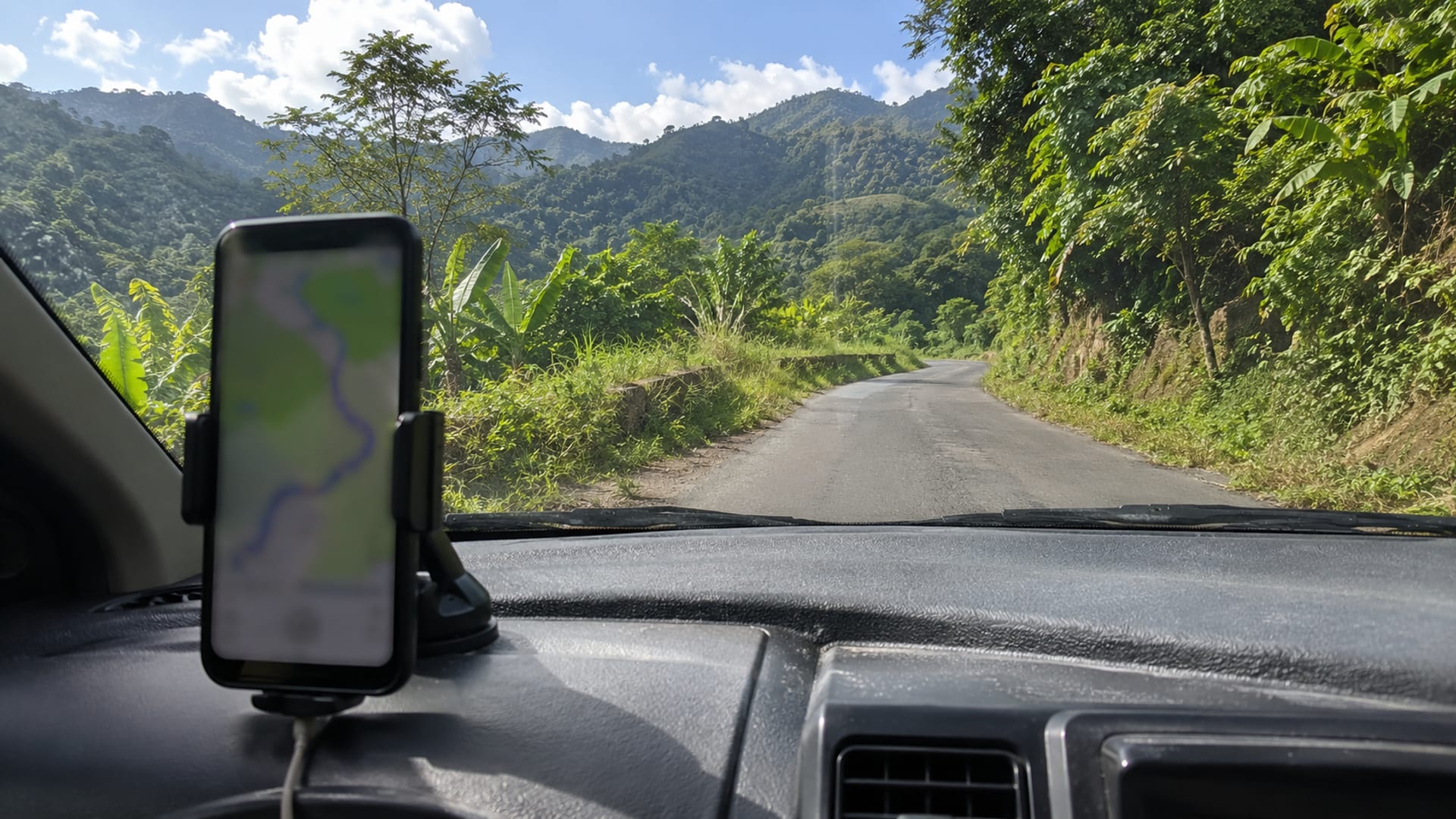 A phone showing a blurred map on a dashboard with a country road ahead