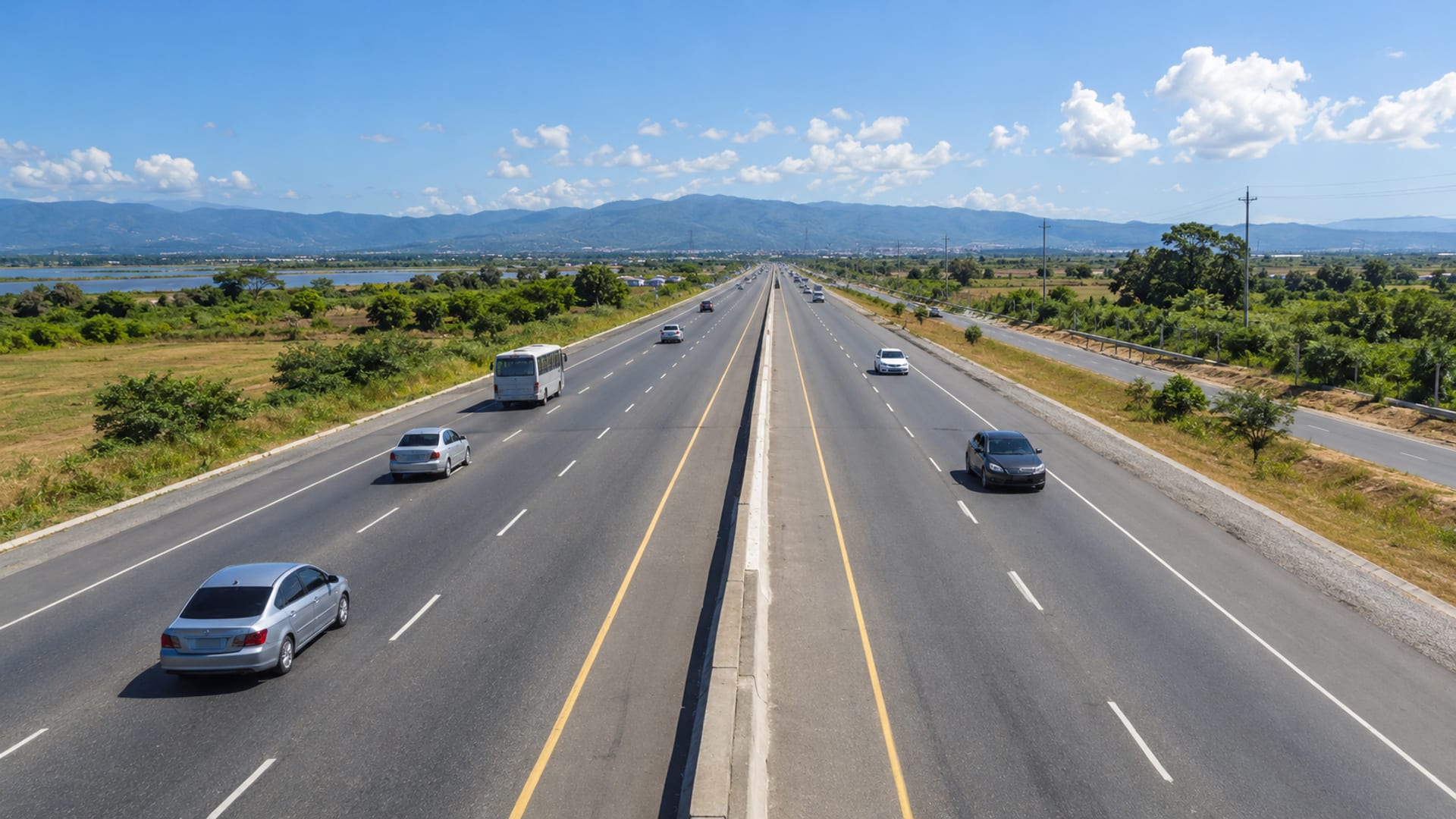 A wide highway crossing flat plains toward low hills with light traffic