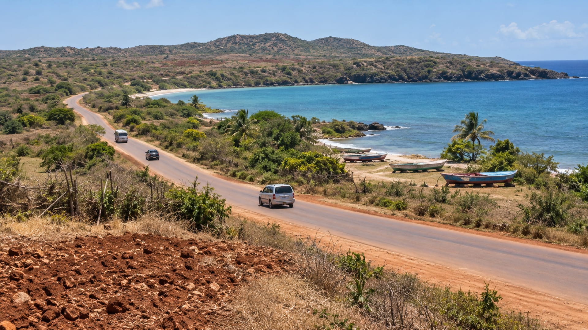 A dry coast road through red earth farmland toward a quiet bay