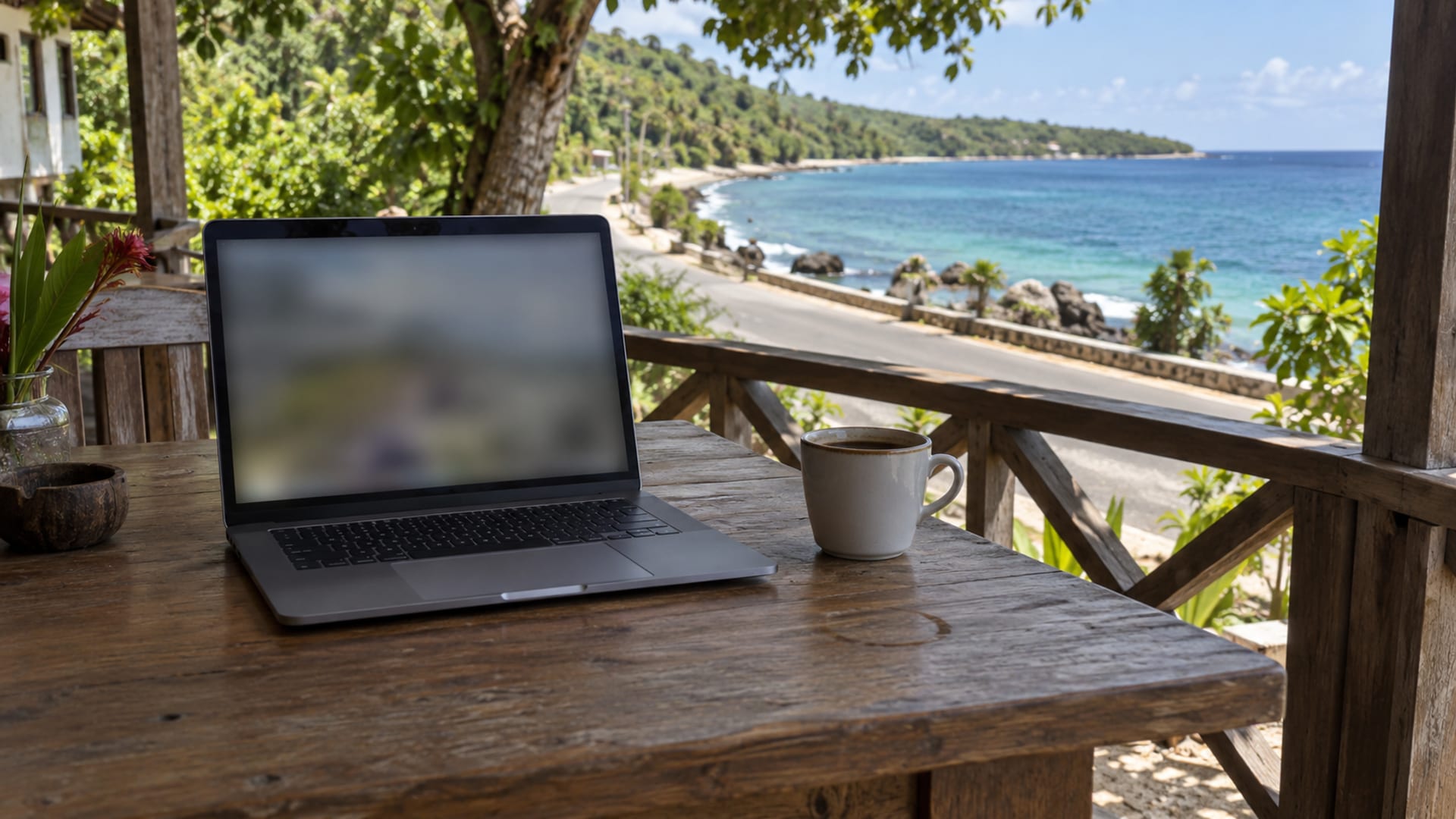 A laptop on a veranda table overlooking a coastal road